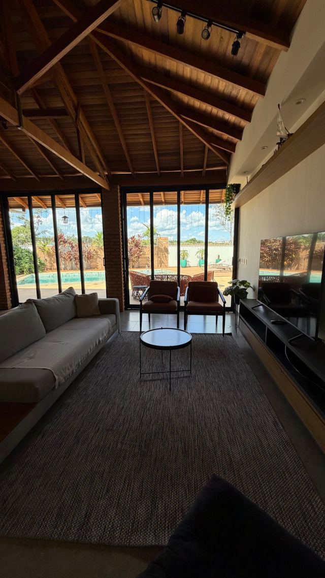 Sala de estar com TV, sofá e portas de vidro para a piscina